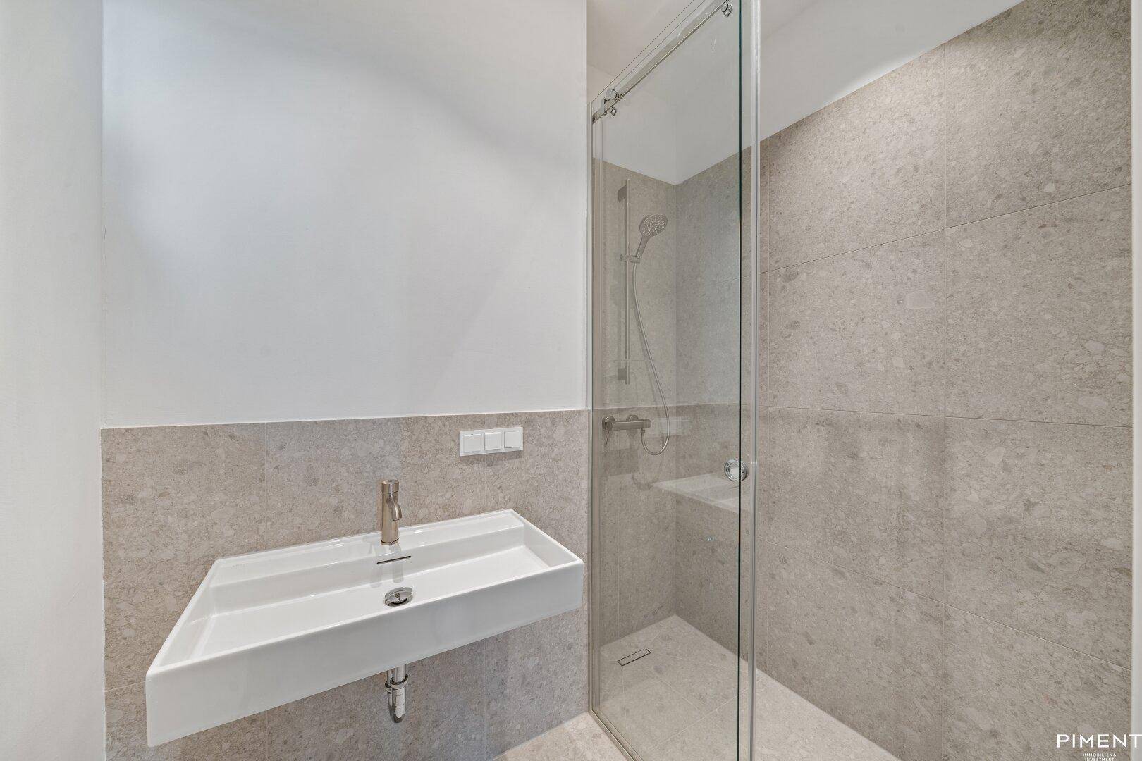 Zeitgemäßes Badezimmer mit großformatigen grauen Fliesen, Duschkabine und modernem Waschtisch.