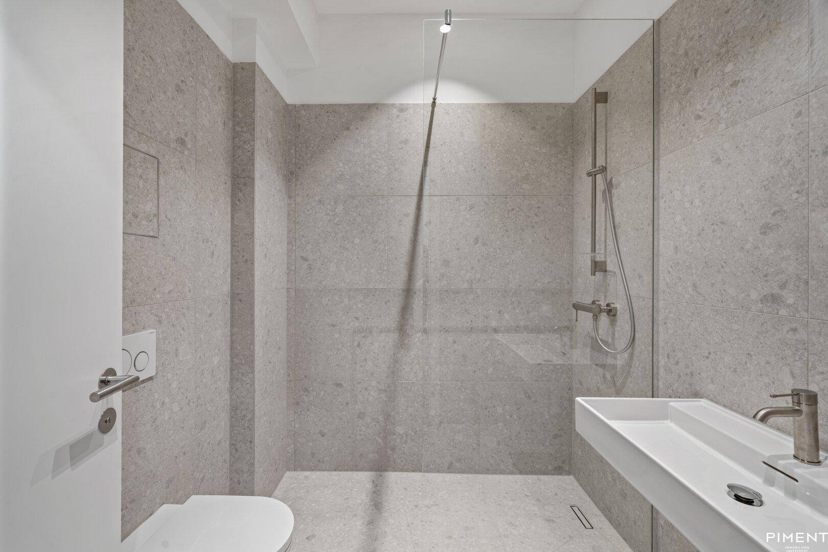 Modernes Badezimmer mit grauen Fliesen, ebenerdiger Dusche und wandhängendem WC.