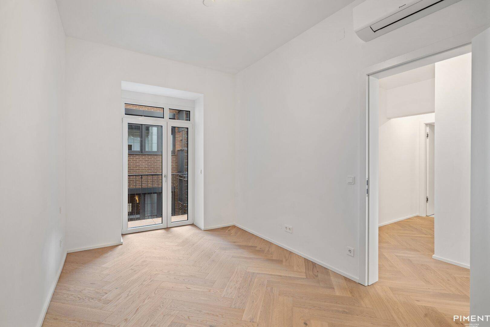 Helles Zimmer mit Fischgrätparkett, Klimaanlage und Zugang zu einem französischen Balkon.