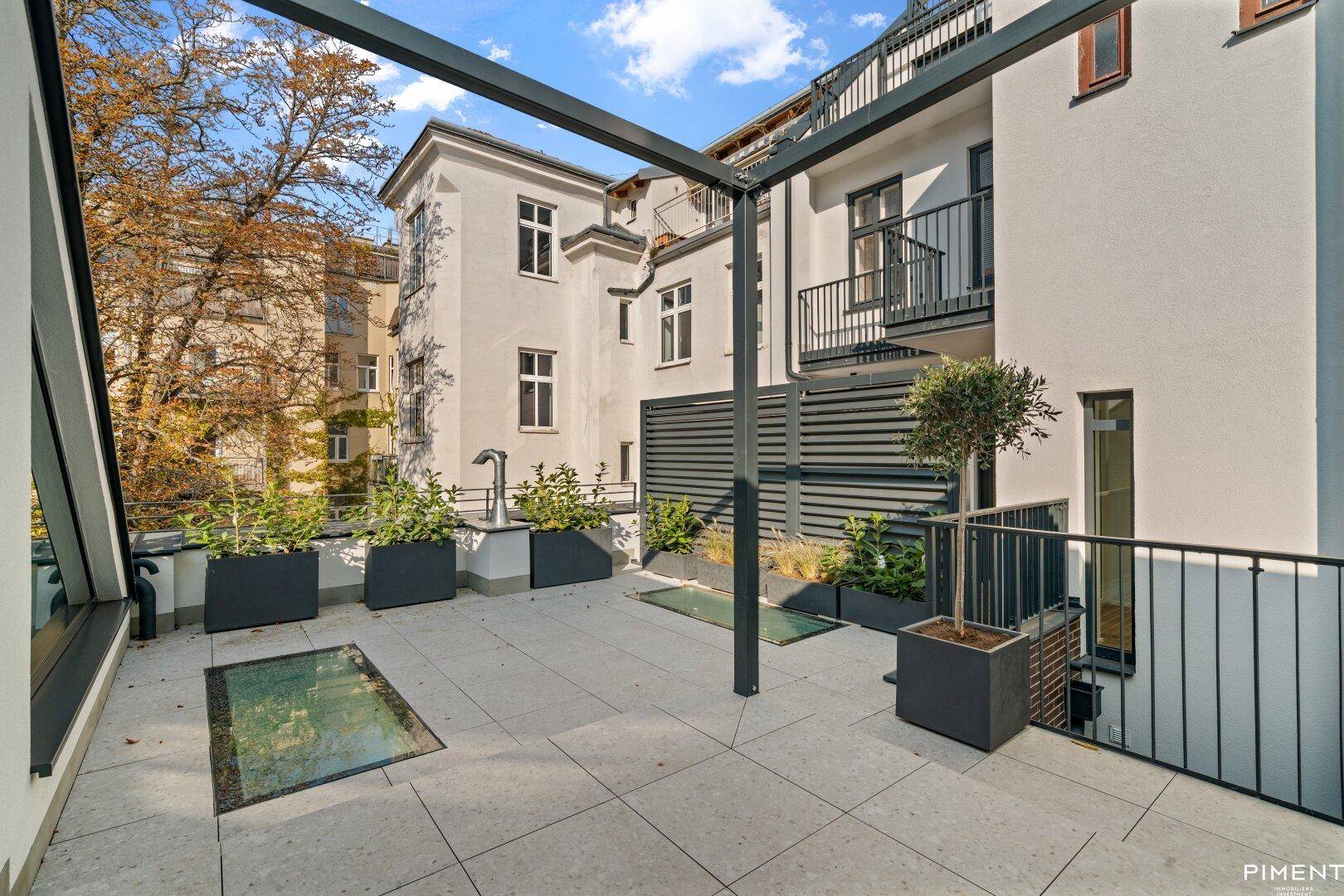 Weitläufige Dachterrasse mit modernen Fliesen, Pflanzenkübeln und Blick auf umliegende Gebäude.