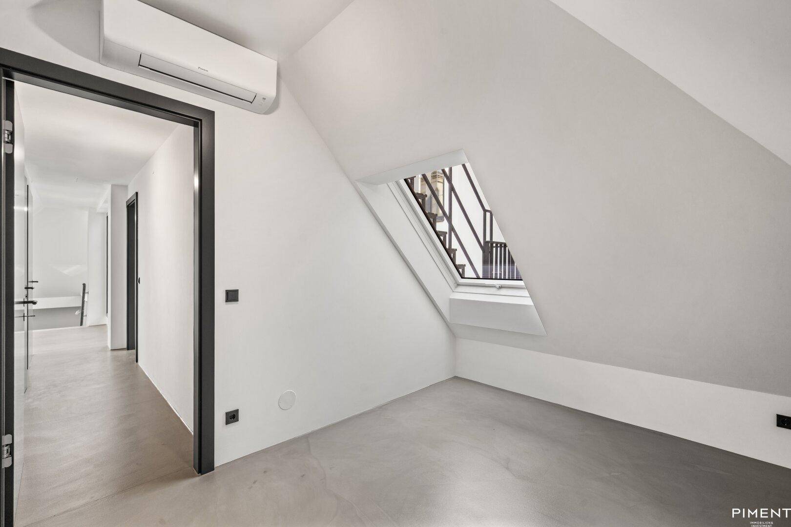 Dachgeschossraum mit schrägen Wänden, Dachfenster, Klimaanlage und Zugang zu einem Flur.