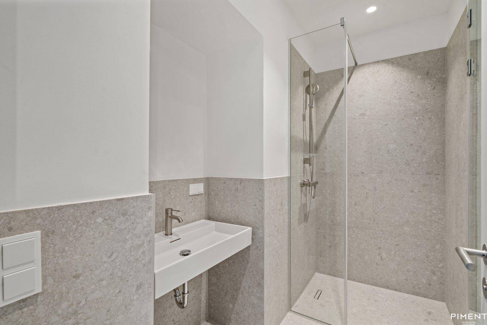 Modernes Badezimmer mit grauen Fliesen, einer ebenerdigen Dusche und einem einzelnen Waschbecken.