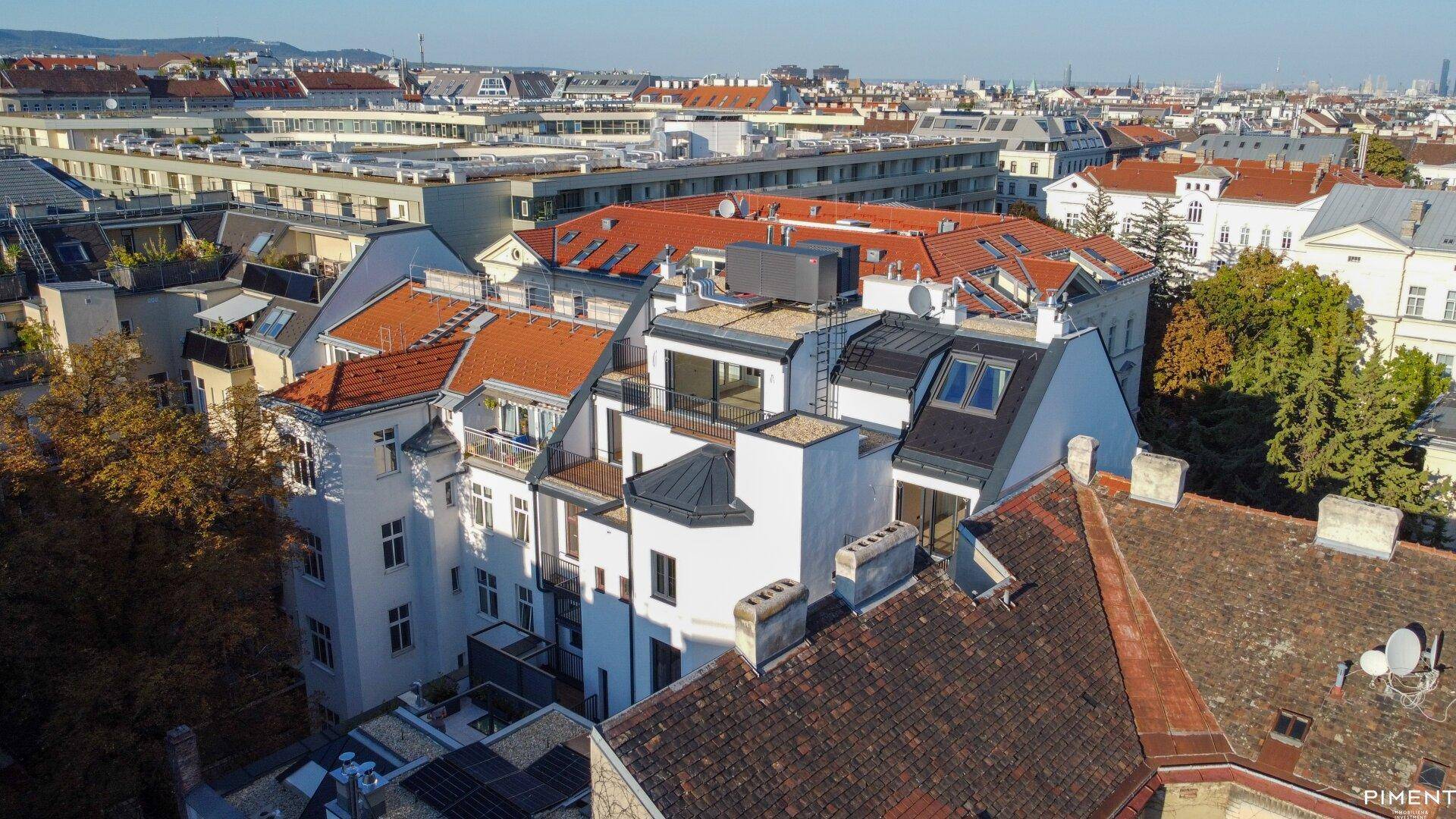 Luftaufnahme eines Wohnblocks mit verschiedenen Dachformen und Blick auf die Stadt.