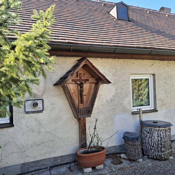 Hausfassade mit einem traditionellen Holzkreuz und einem Fenster, umgeben von Pflanzen.