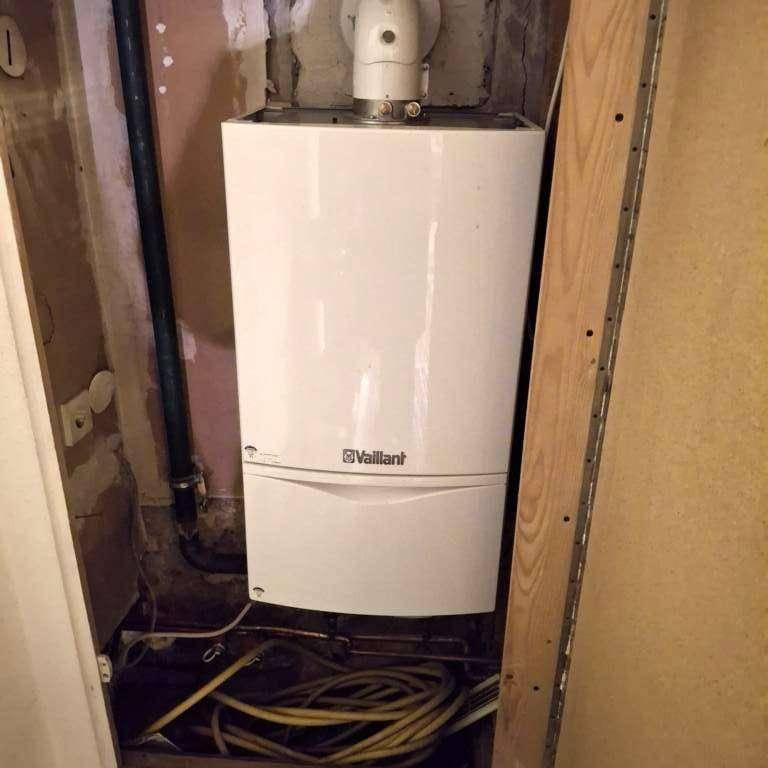 Weißer Vaillant Heizkessel in einem kleinen Technikraum mit sichtbaren Rohren und Kabeln.