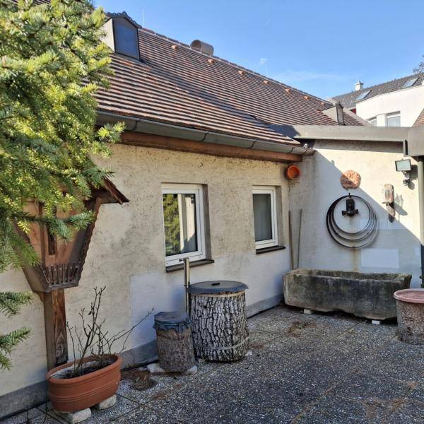 Ecke des Hauses mit zwei Fenstern, einem alten Steintrog und rustikalen Dekorationen.