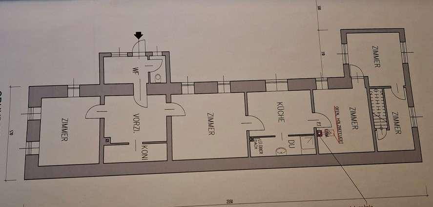 Grundriss einer länglichen Wohnung mit mehreren Zimmern, Küche, Bad und Balkon.