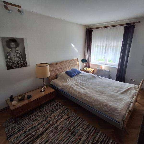 Schlafzimmer mit Doppelbett, Holzboden und einem Fenster mit Vorhängen.