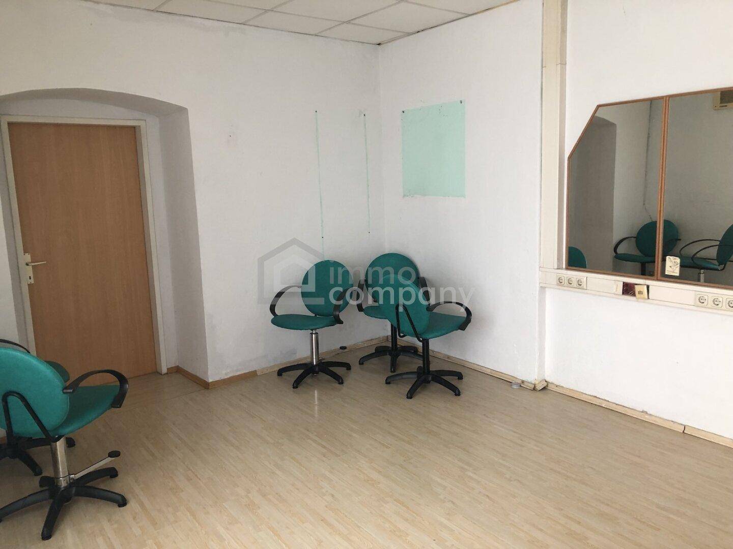 Büroraum mit mehreren Bürostühlen, Laminatboden, Spiegel an der Wand und abgehängter Decke.