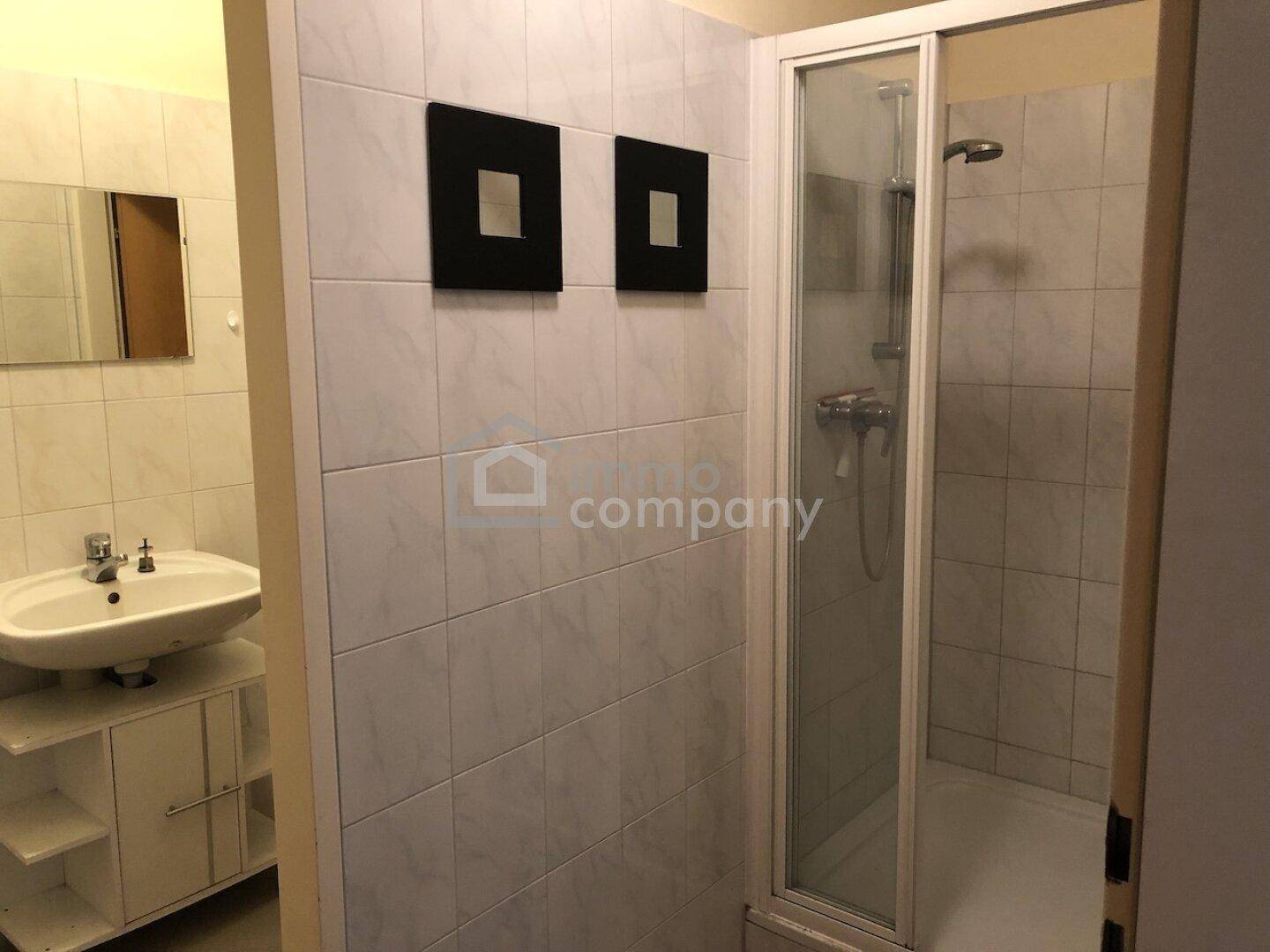 Helles Badezimmer mit Duschkabine, Waschbecken und weißen Fliesen, funktional eingerichtet.