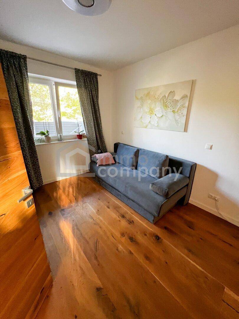 Helles Zimmer mit Holzboden, bequemer Couch und Blick ins Grüne durch das Fenster.