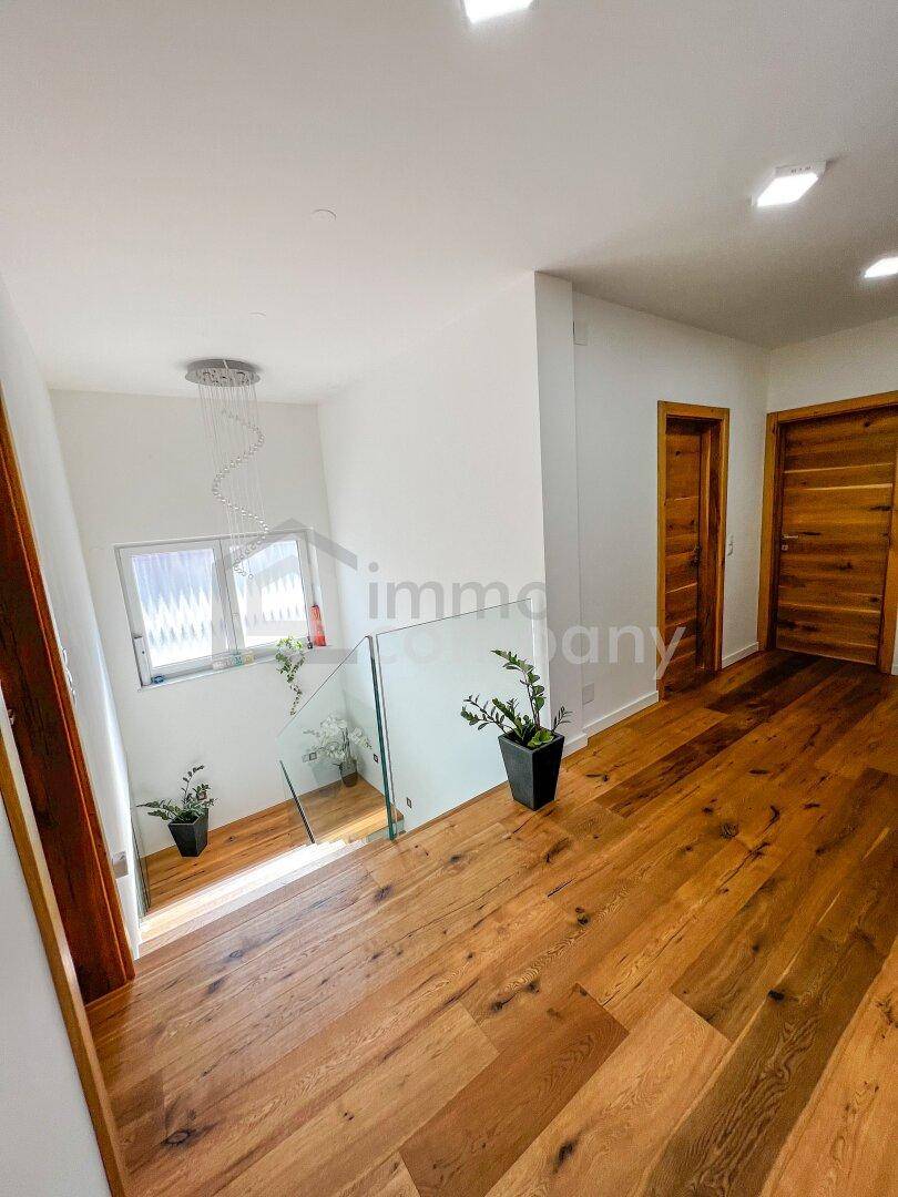 Heller Flur mit Holztreppe, Glasgeländer und Holztüren, der zu weiteren Räumen führt.