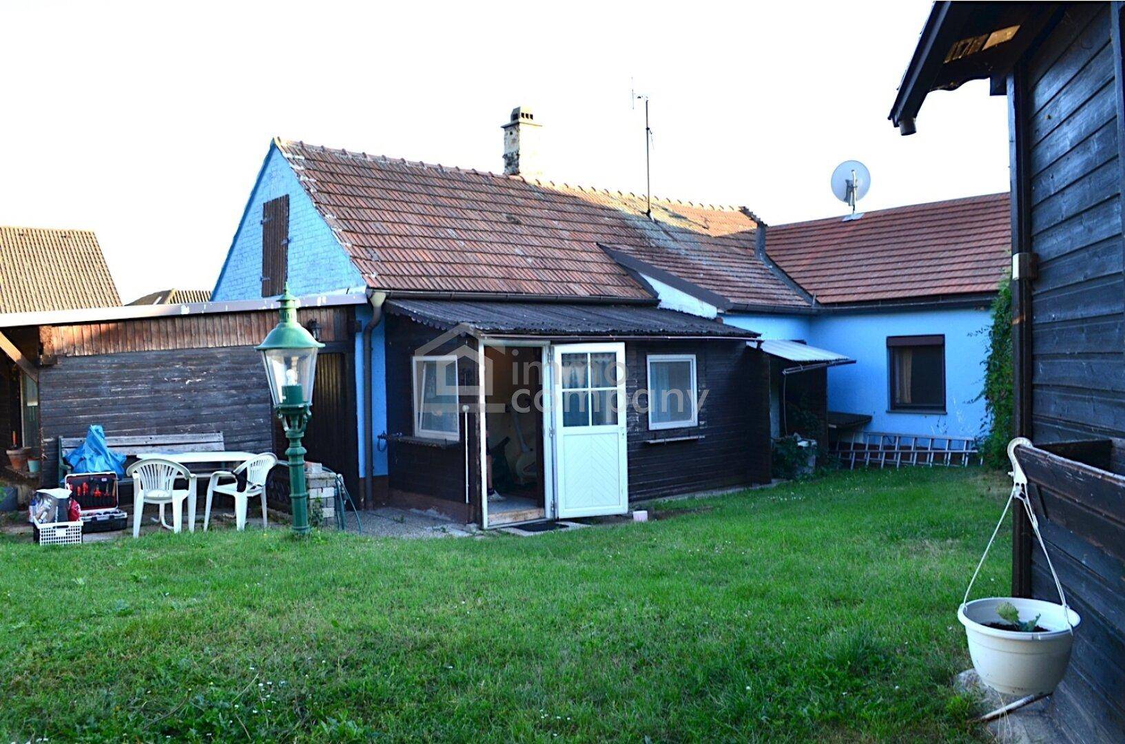 Hinteransicht des Hauses mit kleinem Gartenbereich und einfacher Sitzgelegenheit im Freien.