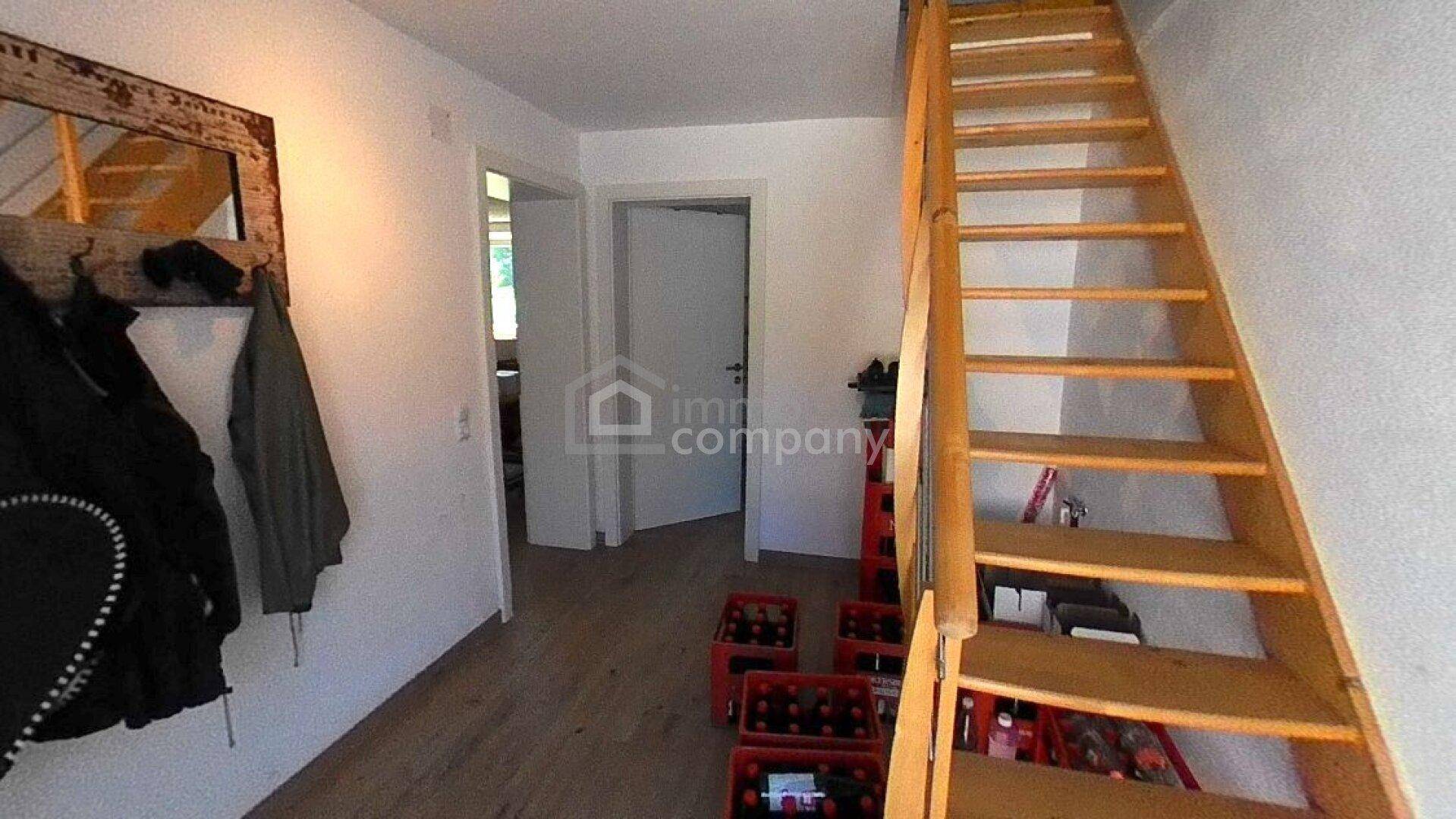 Heller Flur mit Holztreppe, die in das obere Stockwerk führt, und Laminatboden.