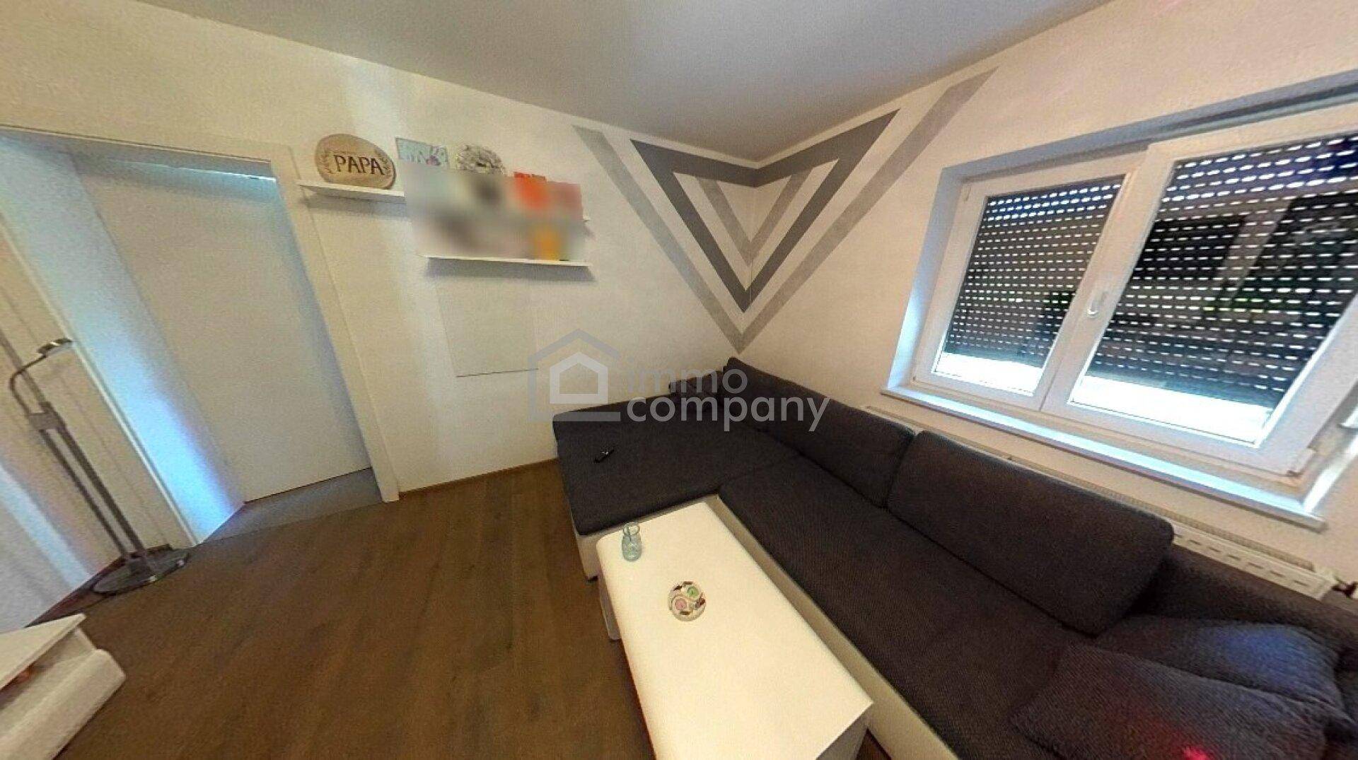 Wohnzimmer mit modernem Ecksofa, Couchtisch und Fenster mit geschlossenen Rollläden.