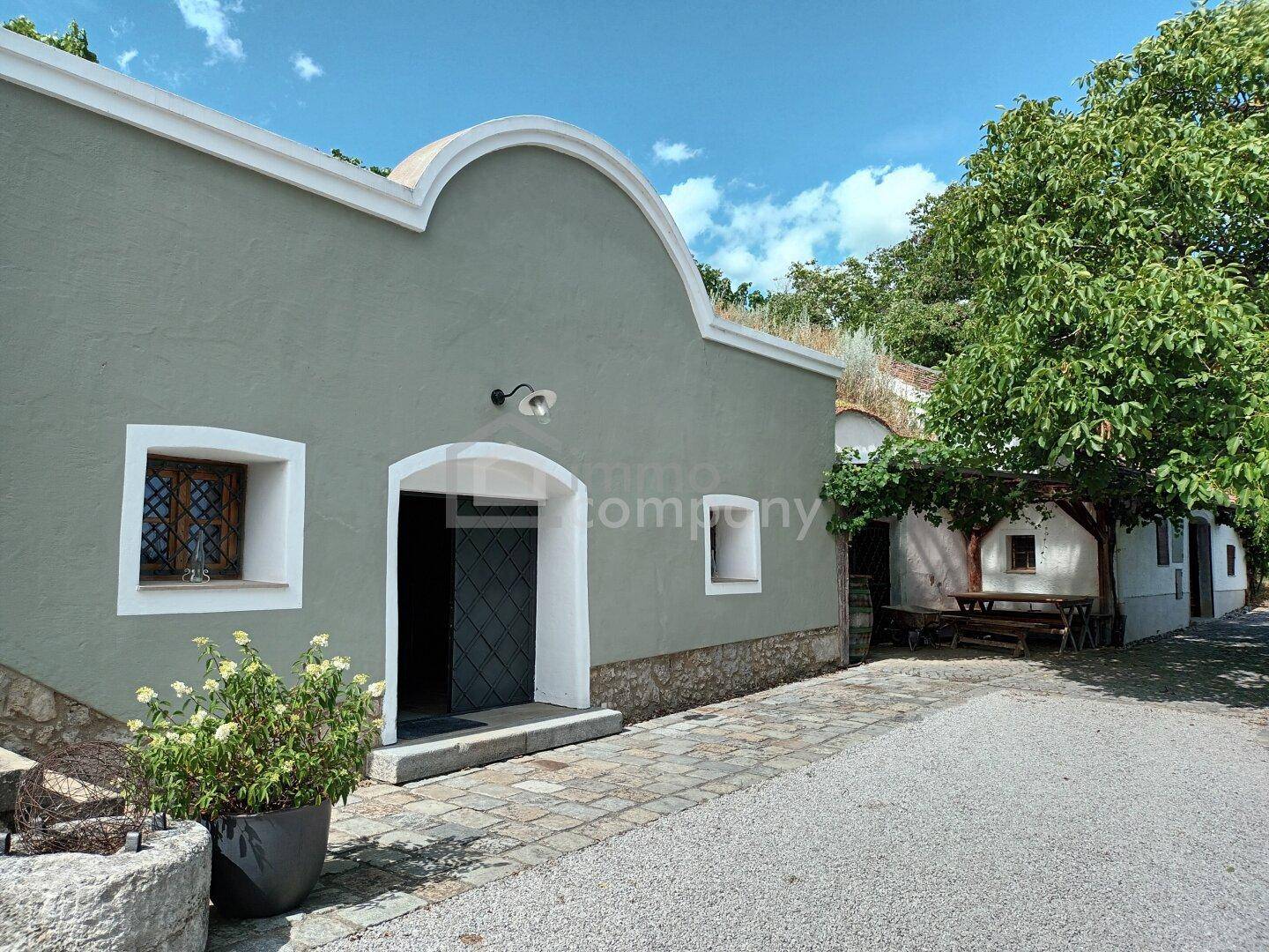 Traditionelles Gebäude mit geschwungener Fassade, begrüntem Dach und gepflastertem Eingangsbereich.