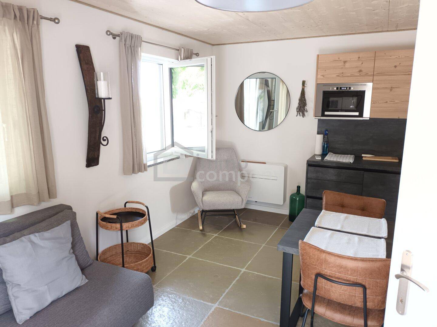 Heller Wohn-Essbereich mit kleiner Küchenzeile, Sofa und Fenster mit Blick ins Grüne.