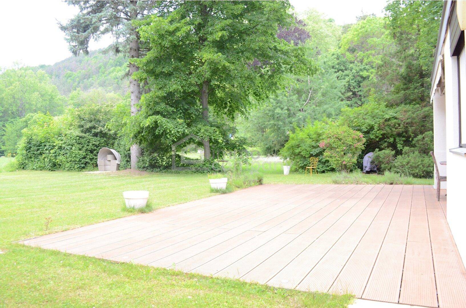 Weitläufiger Gartenbereich mit einer Holzterrasse, umgeben von üppigem Grün und Bäumen.