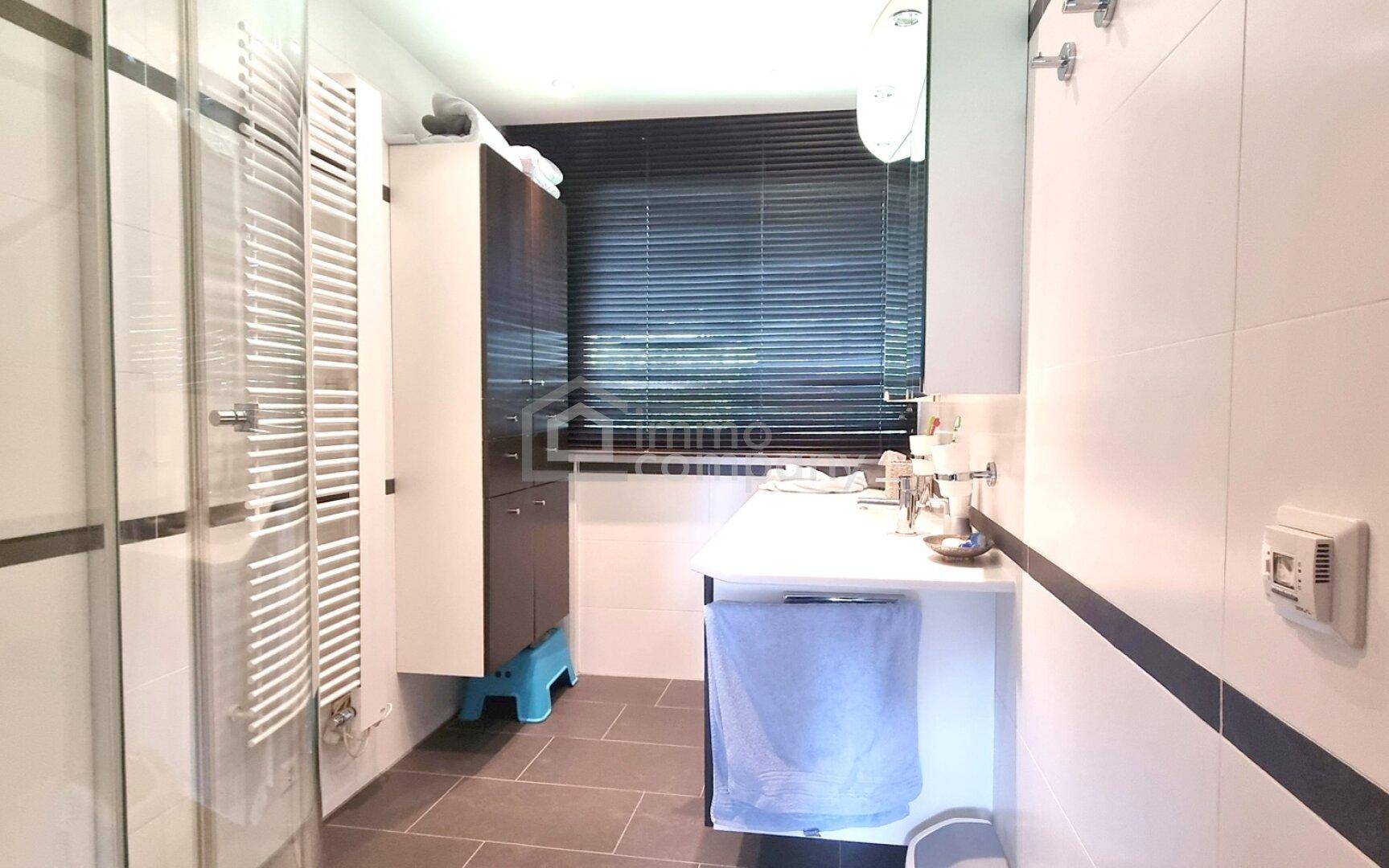 Modernes Badezimmer mit Dusche, beheiztem Handtuchhalter und dunklen Bodenfliesen.