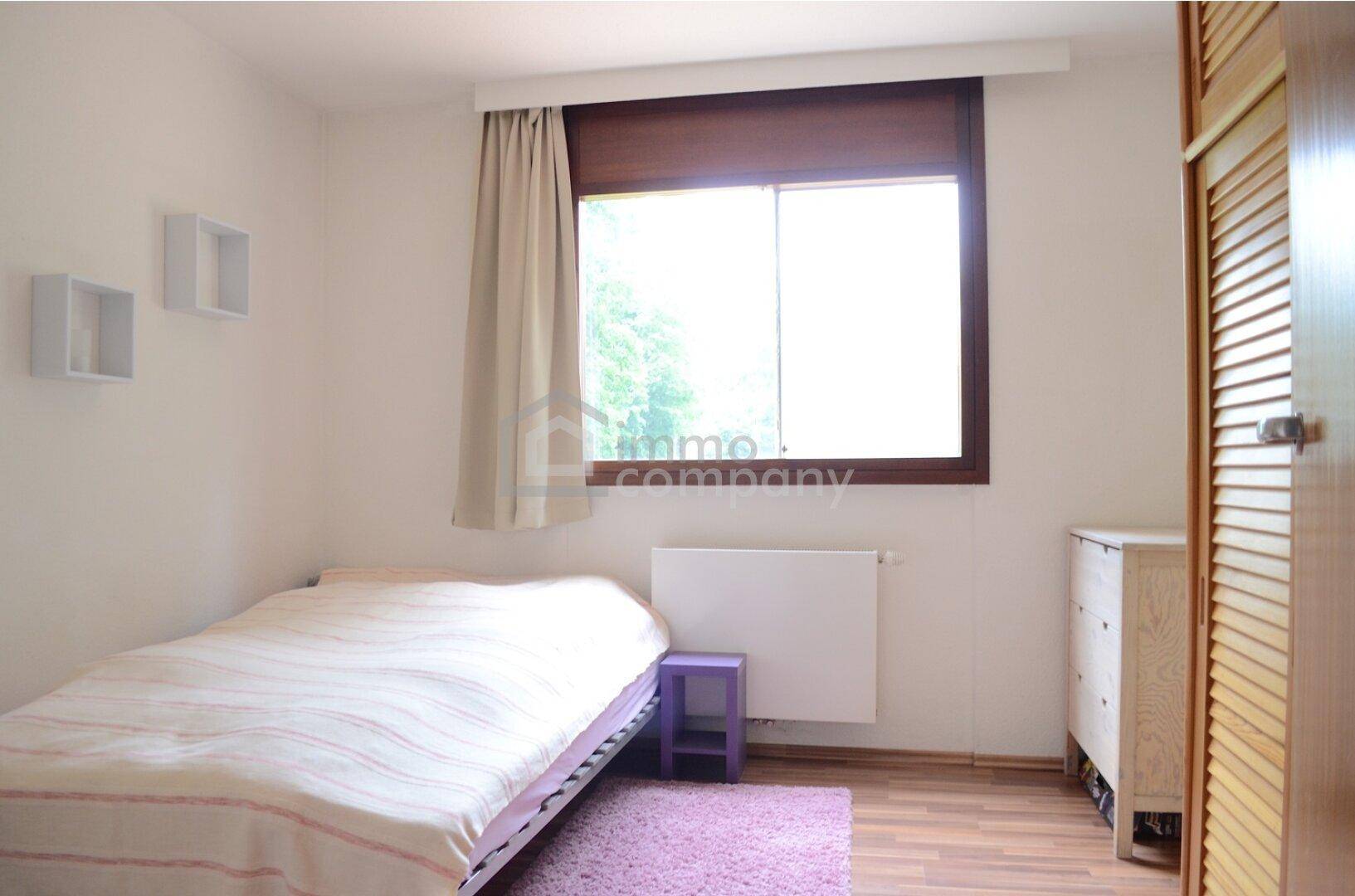 Helles Schlafzimmer mit Einzelbett, Holzboden und Fenster mit Blick ins Grüne.