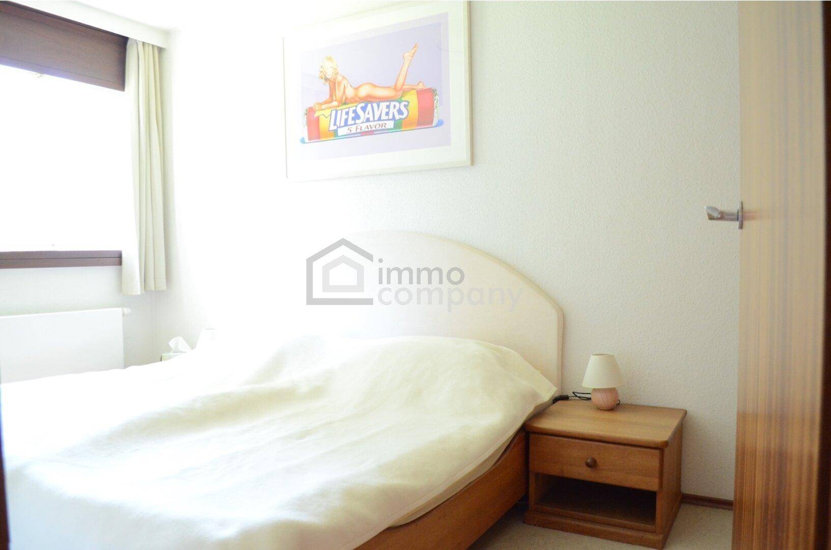 Helles Schlafzimmer mit Doppelbett, Nachttisch und Fenster mit Blick nach draußen.