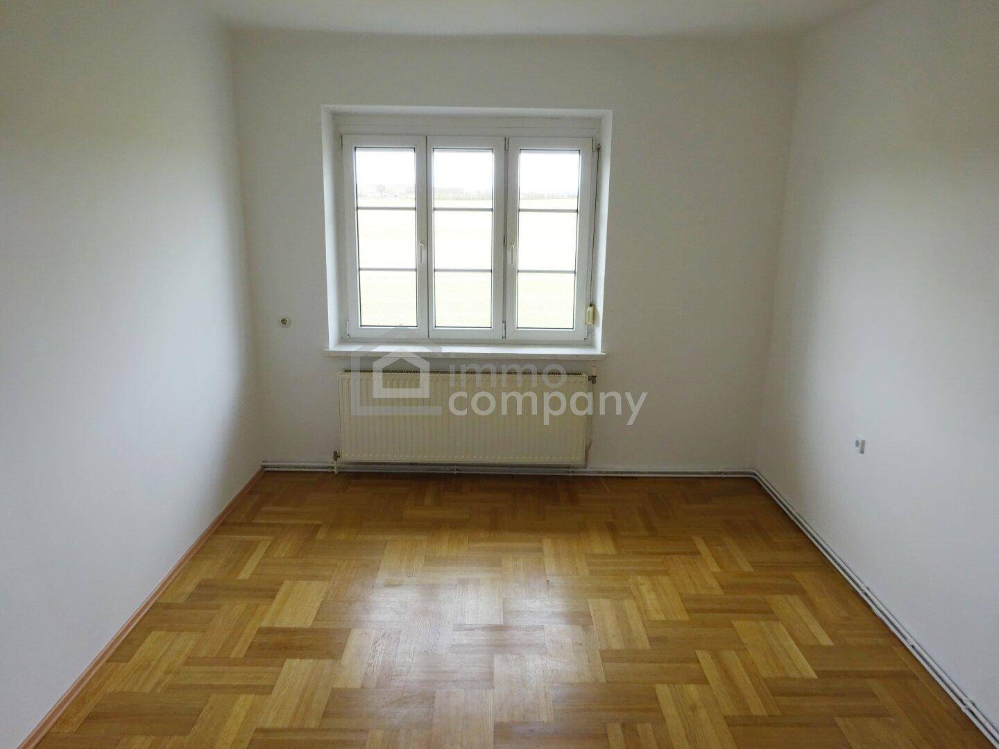 Helles Zimmer mit Parkettboden, weißen Wänden und einem Fenster, bereit zur Einrichtung.