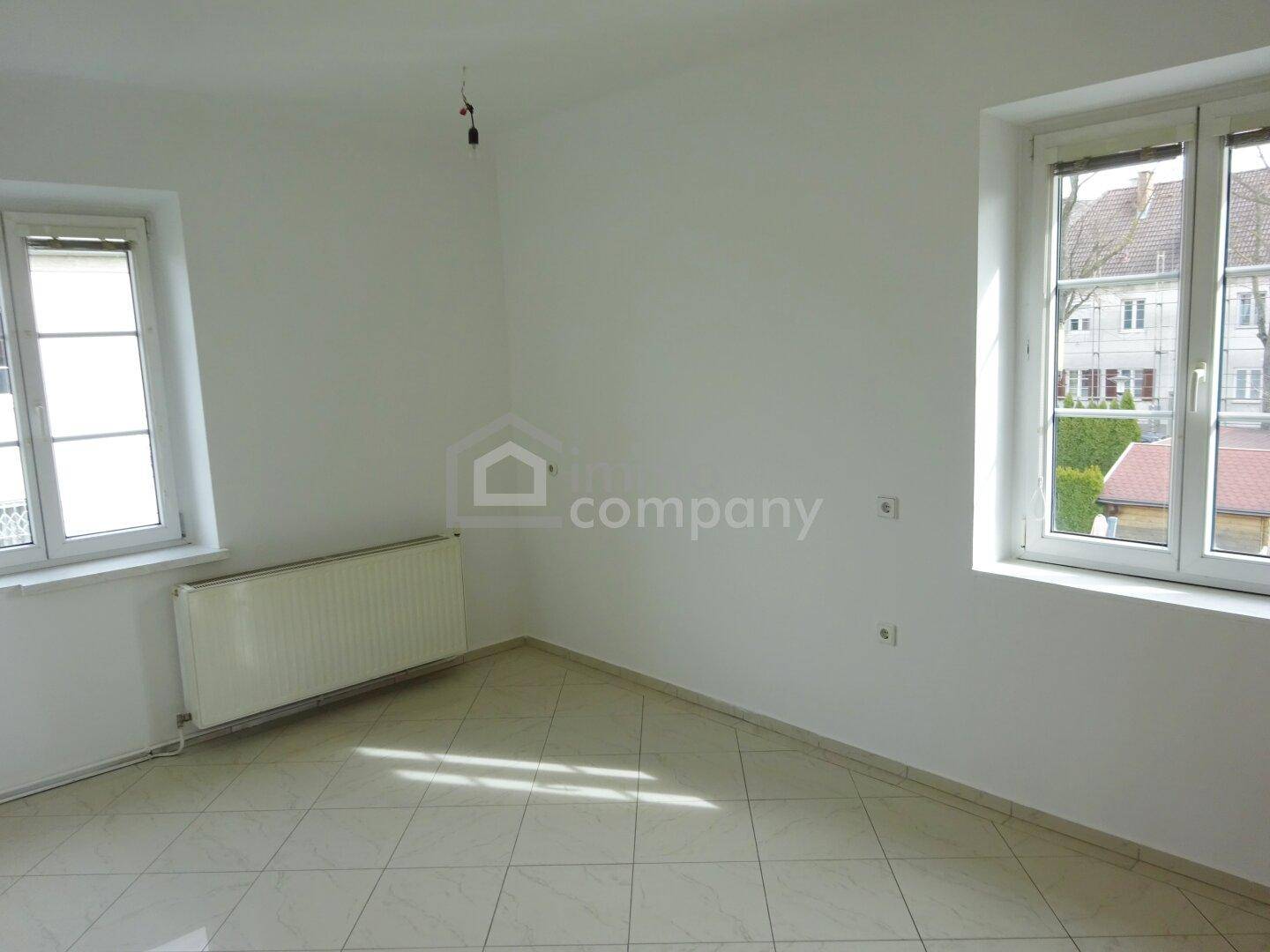 Geräumiges Zimmer mit Fliesenboden, weißen Wänden und zwei großen Fenstern.