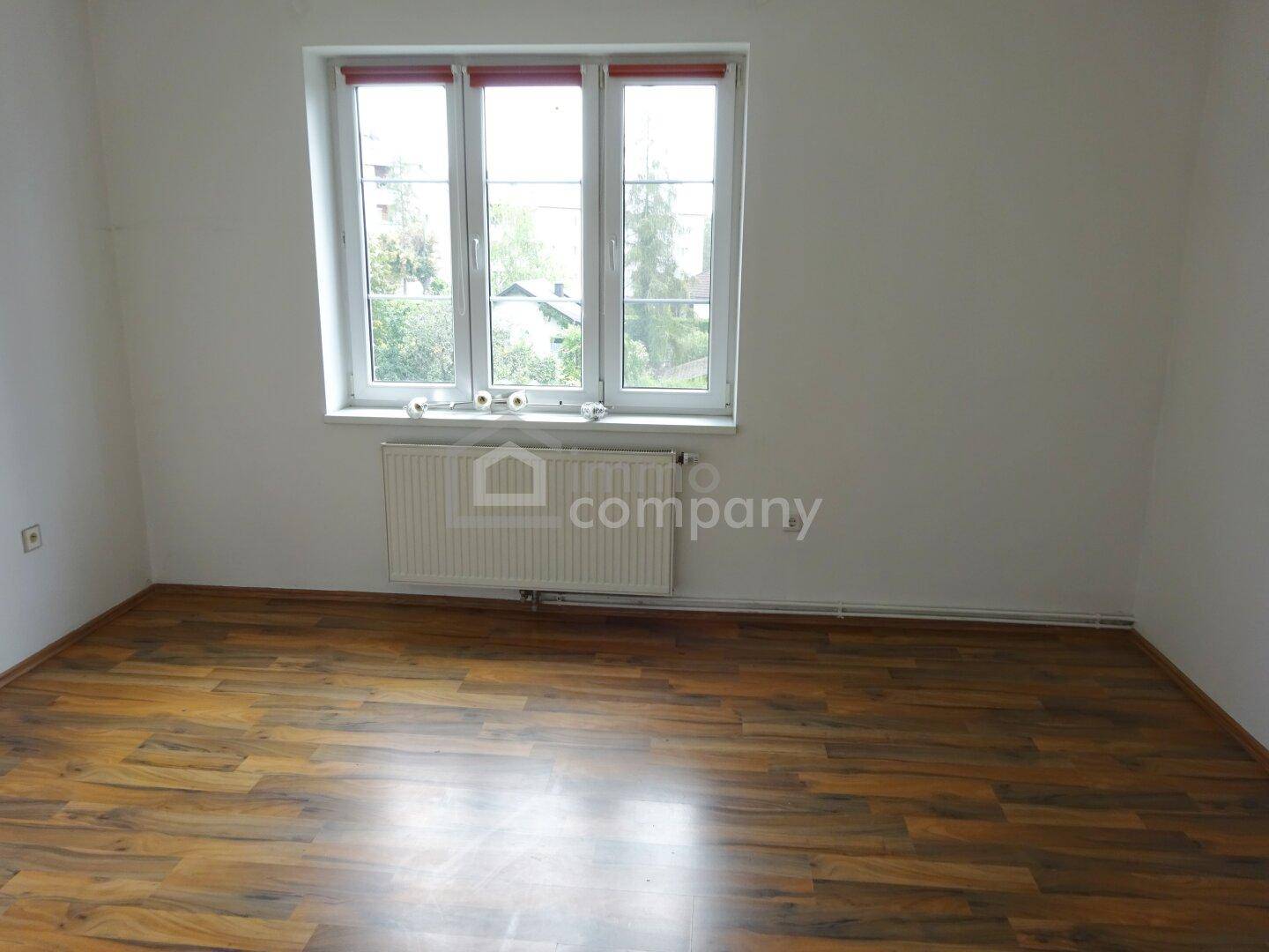 Helles, leeres Zimmer mit großem Fenster und ansprechendem Laminatboden, ideal als Schlafzimmer nutzbar.
