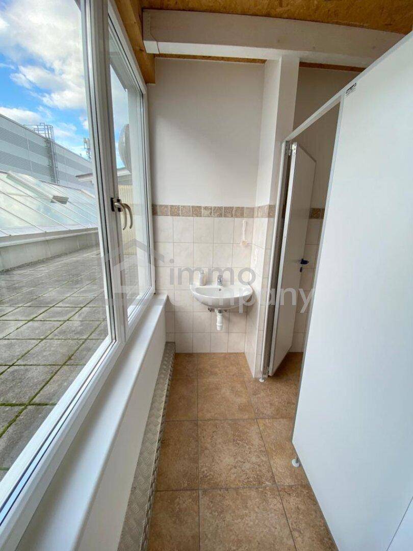 Kleiner Toilettenbereich mit Waschbecken, gefliesten Wänden und einem Fenster mit Blick auf eine Dachterrasse.