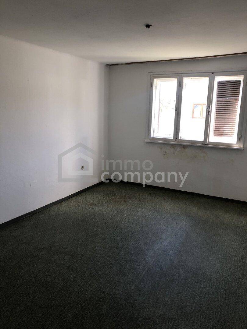 Leerer Raum mit Teppichboden und Fenster, das Tageslicht hereinlässt.