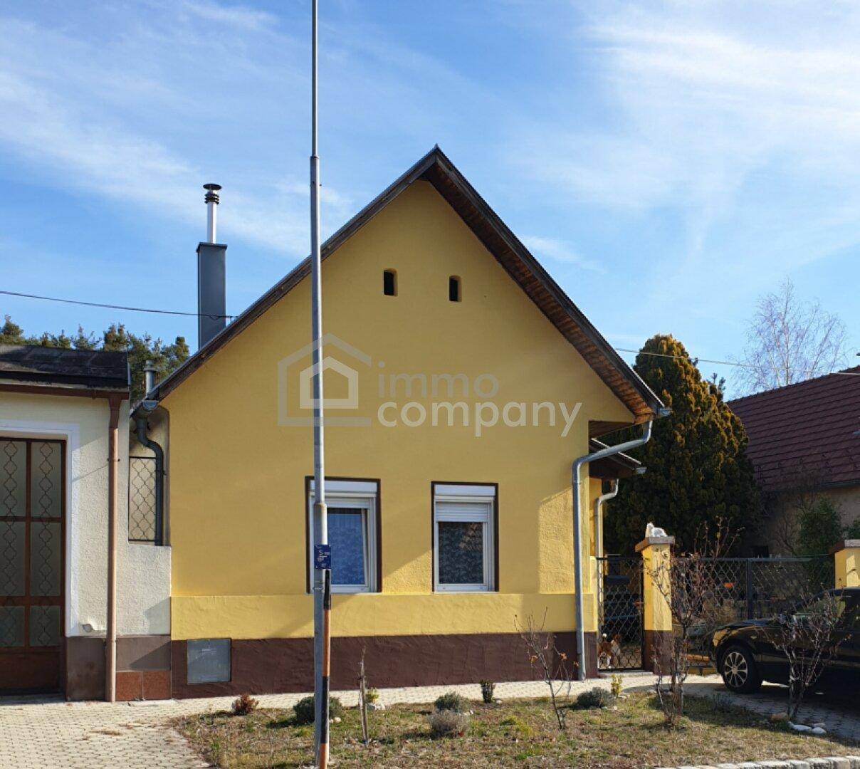 Gelbes Einfamilienhaus mit braunem Sockel und Satteldach unter blauem Himmel.