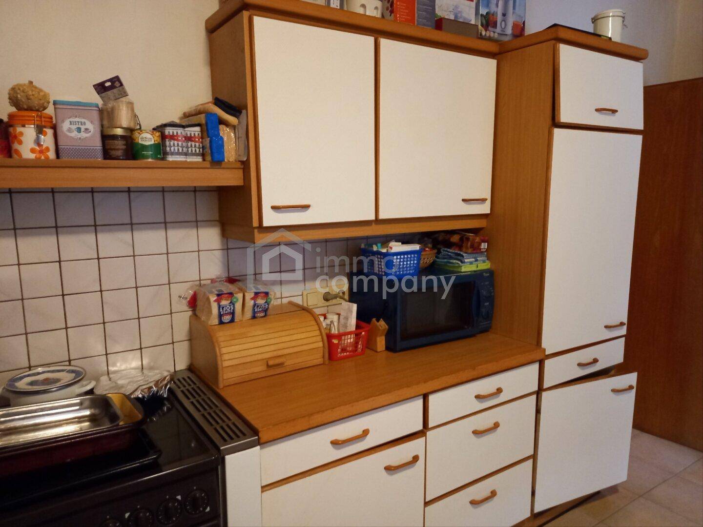 Funktionale Küche mit Holzschränken, weißen Fronten und gefliestem Spritzschutz.