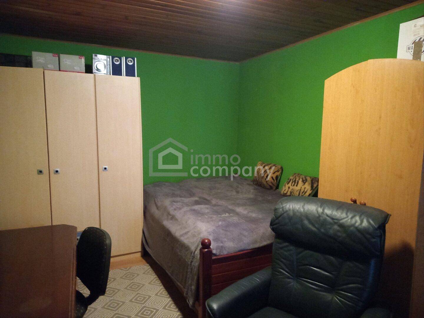 Schlafzimmer mit grünen Wänden, Holzbett, Kleiderschrank und Schreibtisch.
