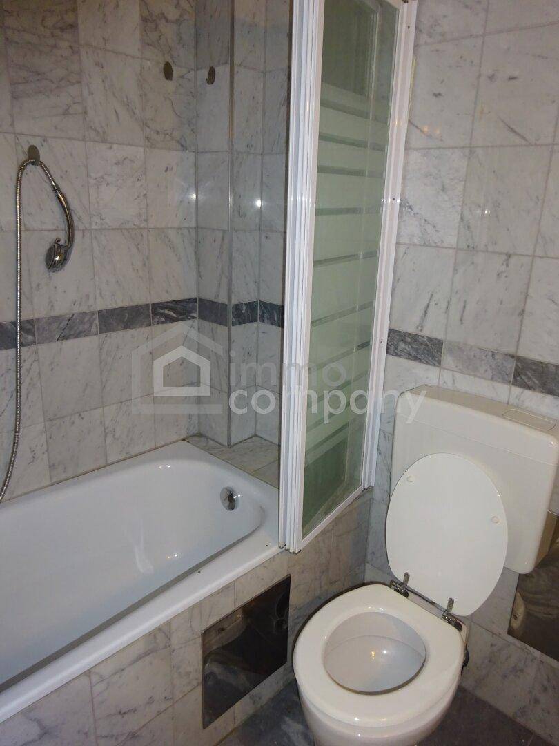 Badezimmer mit Marmorfliesen, Badewanne mit Duschwand und einer Toilette.