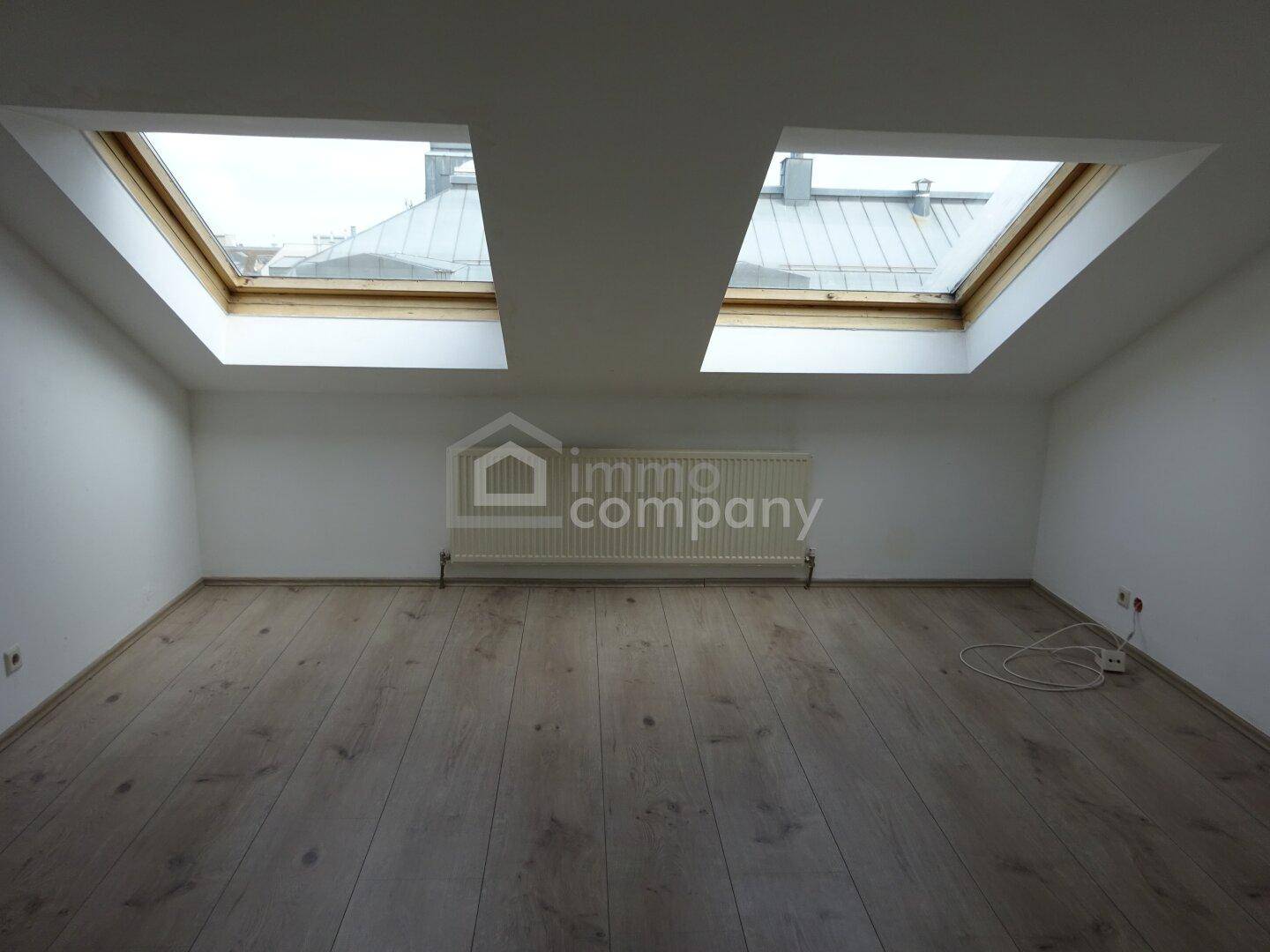 Heller Dachbodenraum mit Holzboden und zwei großen Dachfenstern, die viel Licht hereinlassen.
