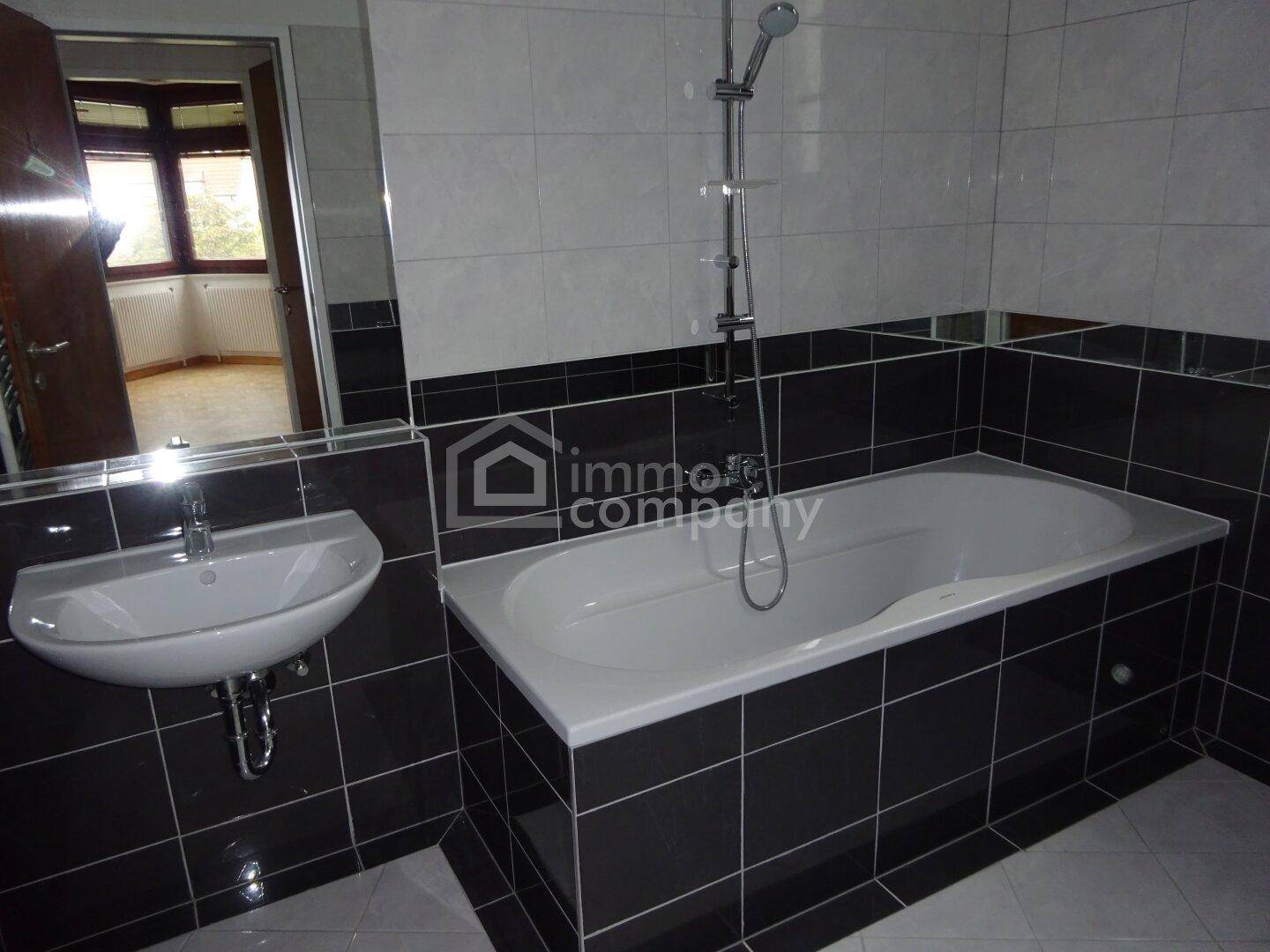 Modernes Badezimmer mit schwarzen und weißen Fliesen, Badewanne, Waschbecken und Spiegel.