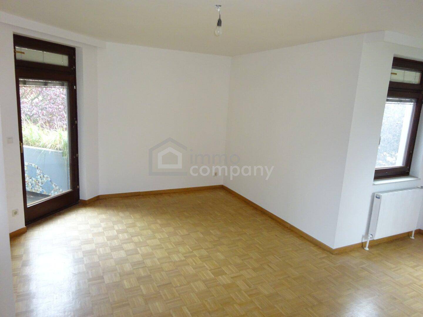 Heller Wohnraum mit Parkettboden, Zugang zu einem Balkon und einem weiteren Fenster.