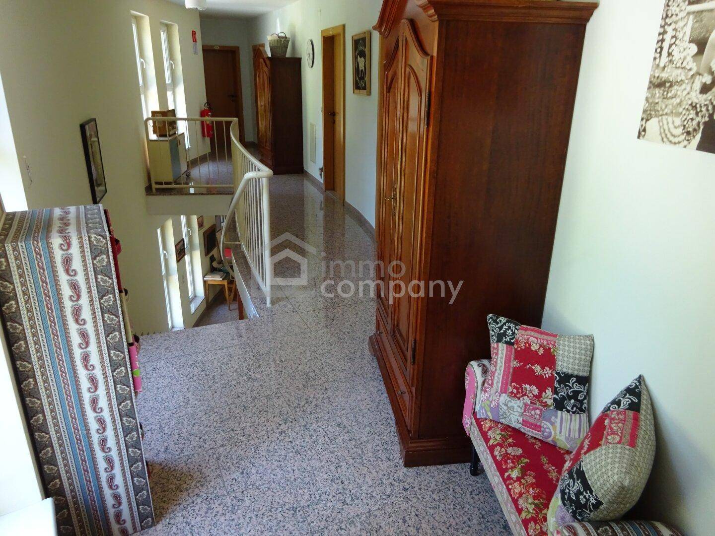 Geräumiger Flur mit Terrazzoboden, Holzschrank und Blick auf eine Treppe.