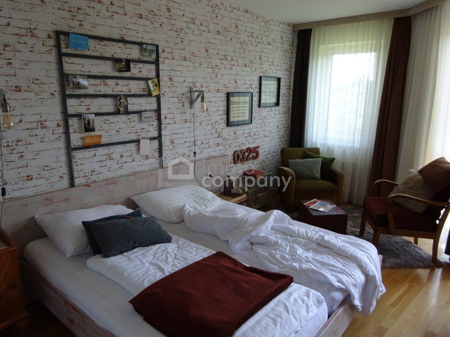 Gemütliches Schlafzimmer mit Ziegelstein-Tapete, Holzboden und bequemen Sesseln.