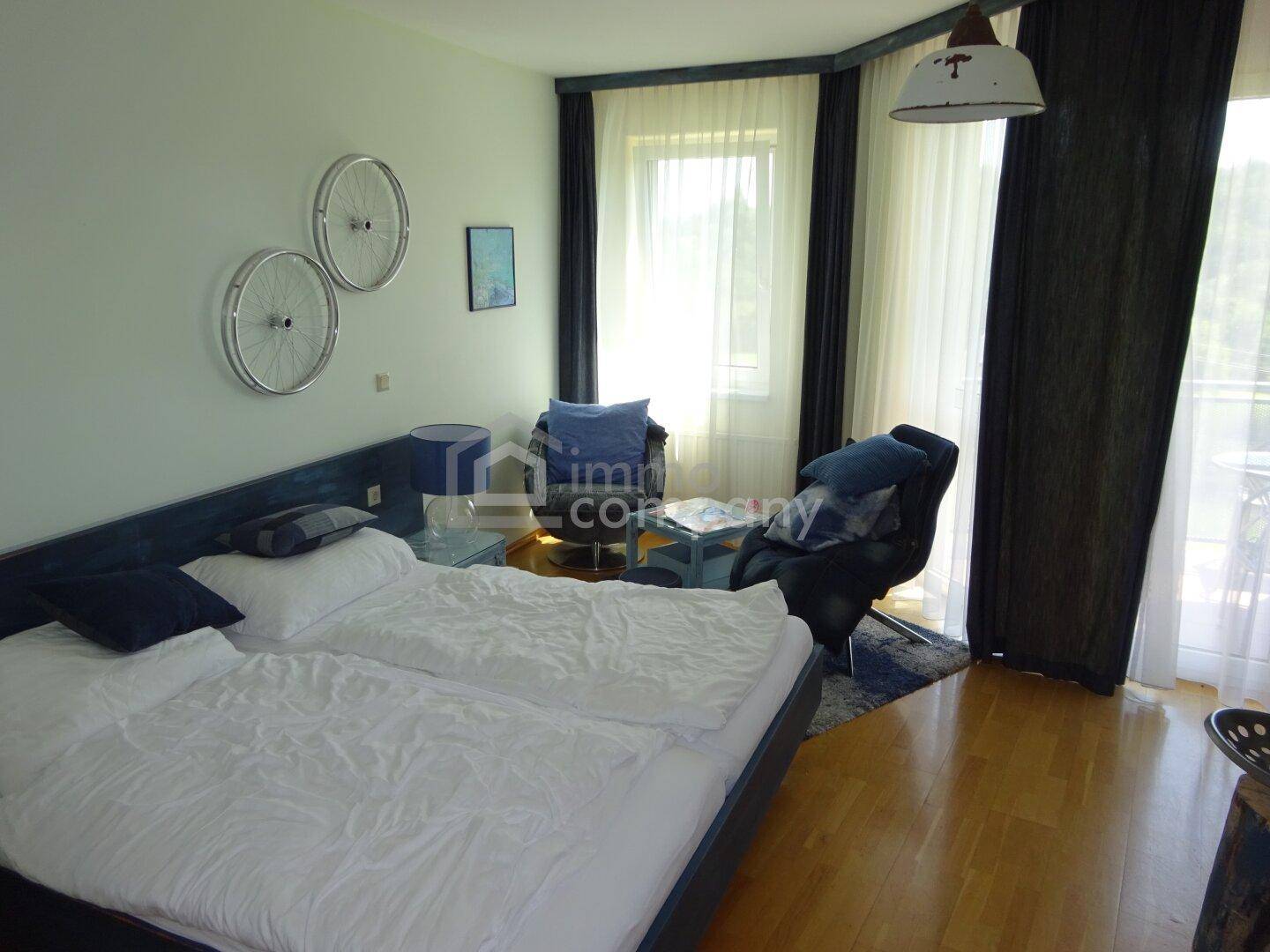 Helles Schlafzimmer mit Holzboden, Doppelbett und Zugang zu einem Balkon.