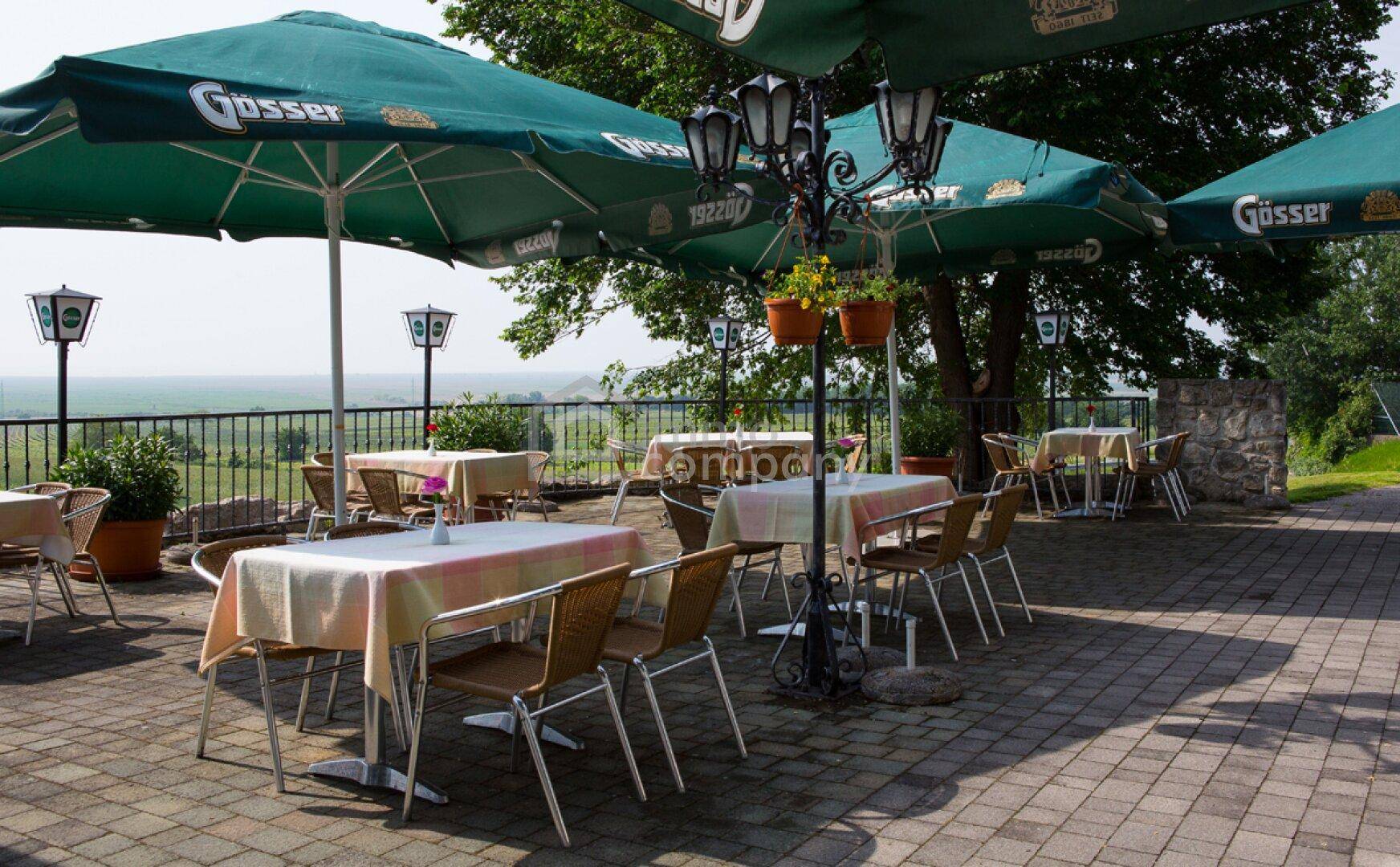 Gemütliche Außenterrasse mit Tischen, Stühlen und großen Sonnenschirmen, bietet einen weiten Blick ins Grüne.
