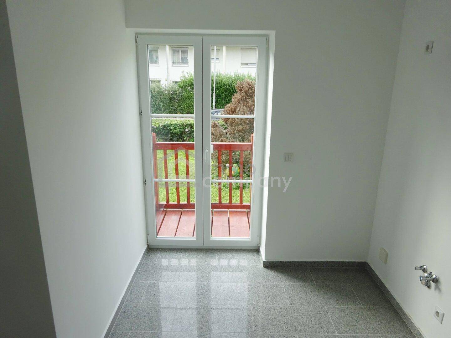 Raum mit grauen Fliesen und Zugang zu einem französischen Balkon mit rotem Geländer.