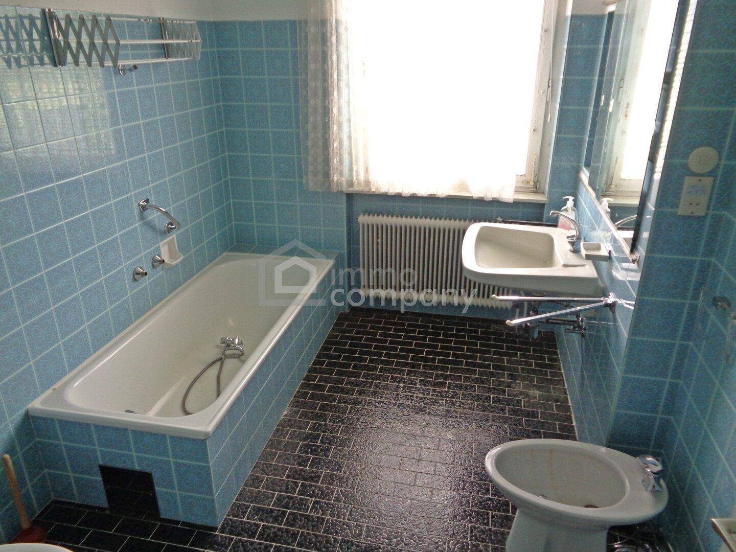 Badezimmer mit blauen Fliesen, Badewanne, Waschbecken und Bidet.