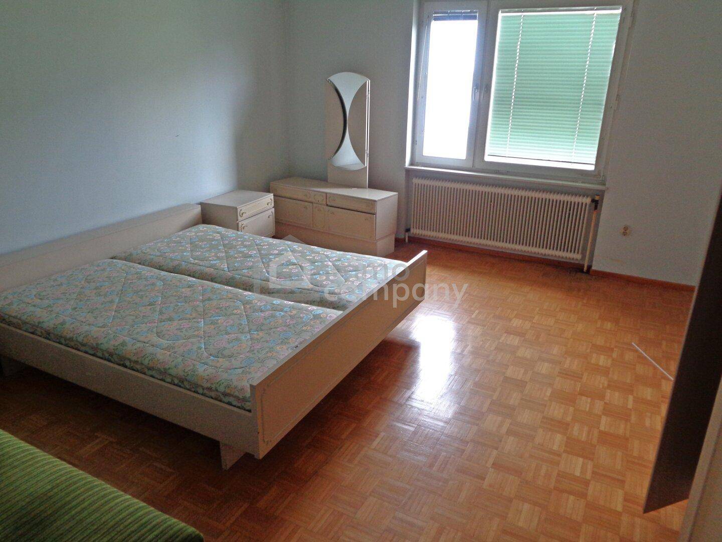 Schlafzimmer mit zwei Einzelbetten, Parkettboden und Fenster mit Jalousien.