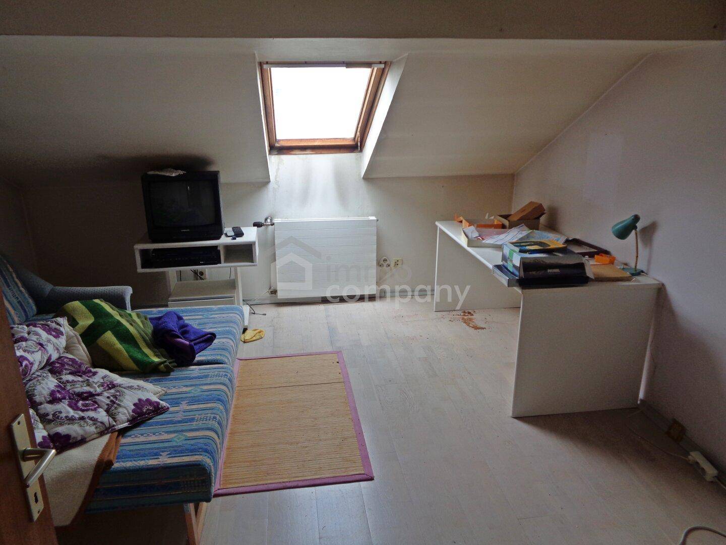 Dachzimmer mit Schreibtisch, Sofa und Dachfenster, ideal als Arbeits- oder Gästezimmer.