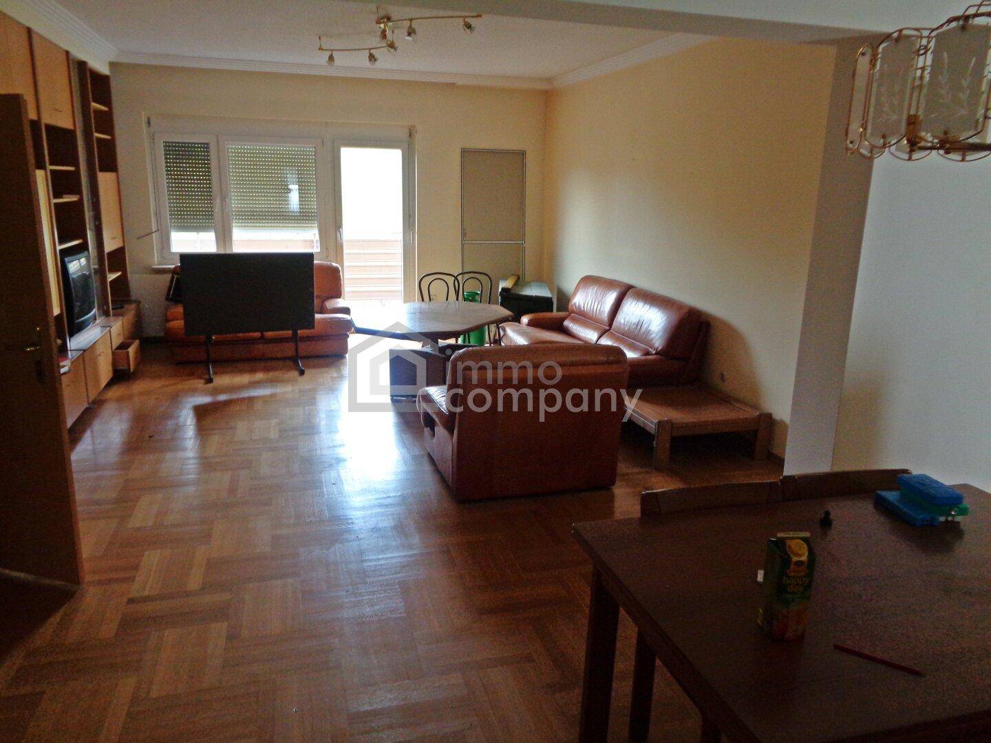 Geräumiger Wohn- und Essbereich mit Parkettboden, Ledersofas und Zugang zum Balkon.