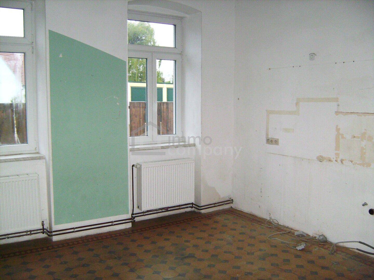 Raum mit grüner Akzentwand, Fenster und Heizkörper, bereit für Renovierungsarbeiten.