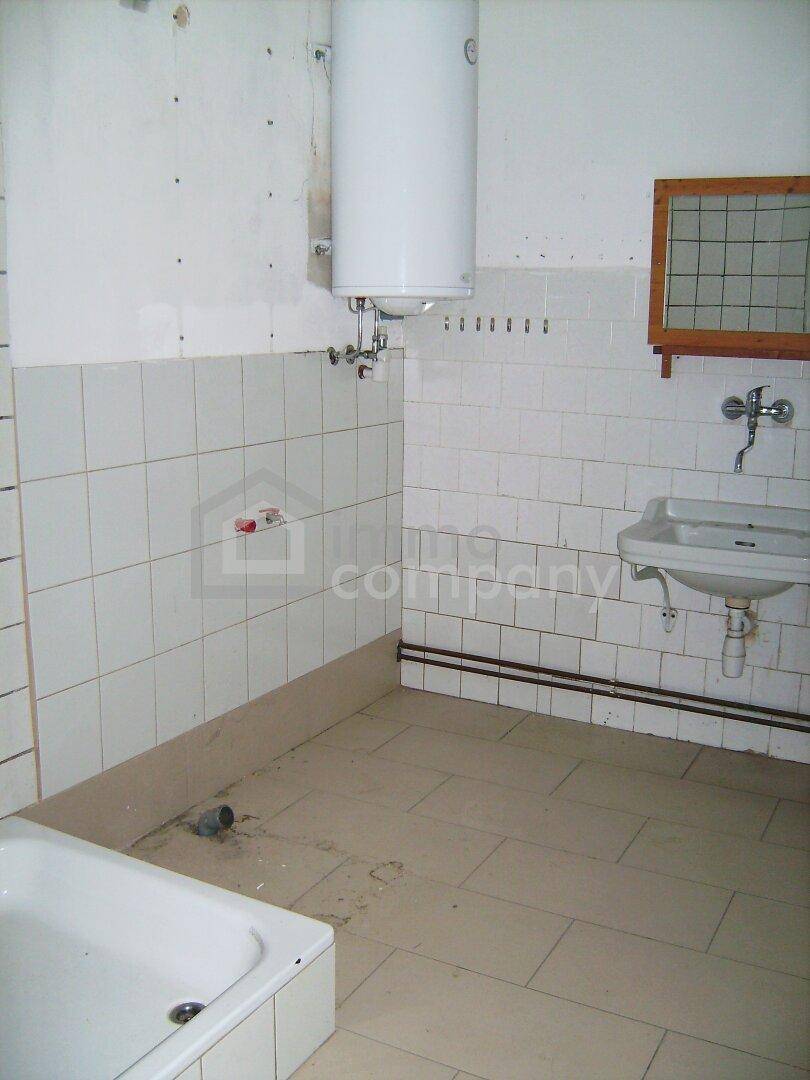 Badezimmer in Renovierung mit Badewanne, Waschbecken und Boiler, ausgestattet mit weißen Fliesen.