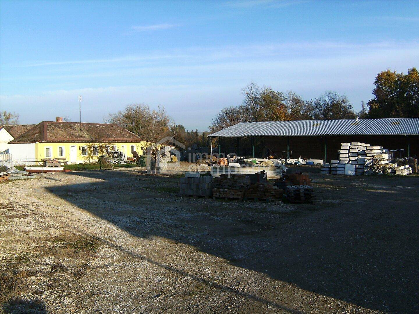 Weitläufiges Grundstück mit einem gelben Wohnhaus und einer großen Lagerhalle im Hintergrund.