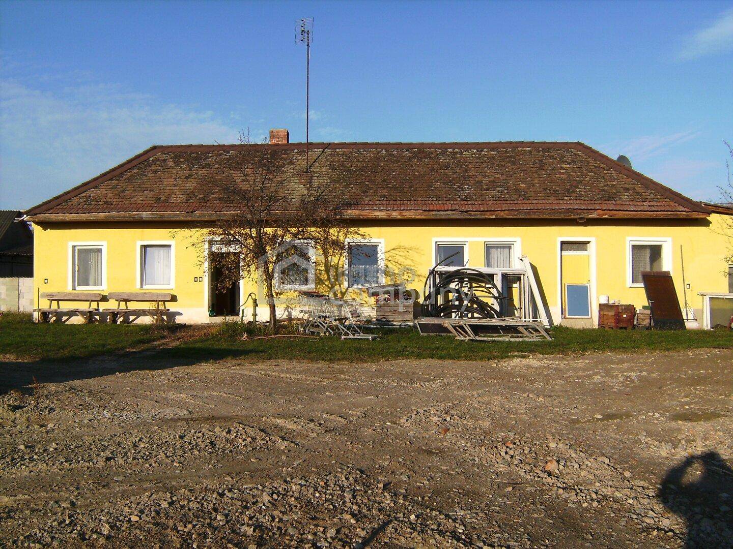 Gelbes Wohnhaus mit rotem Ziegeldach und einem kleinen Vorgartenbereich.